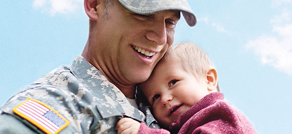 A man wearing miliary fatigues holding a young child to his chest